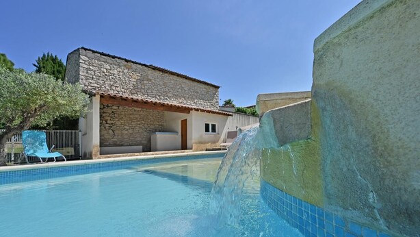 Una piscina con un edificio de piedra al fondo, una silla azul y una fuente de agua.
