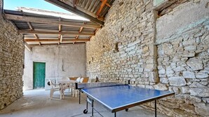 Una mesa de ping pong en una sala rústica con paredes de piedra, una puerta verde y una mesa con sillas.