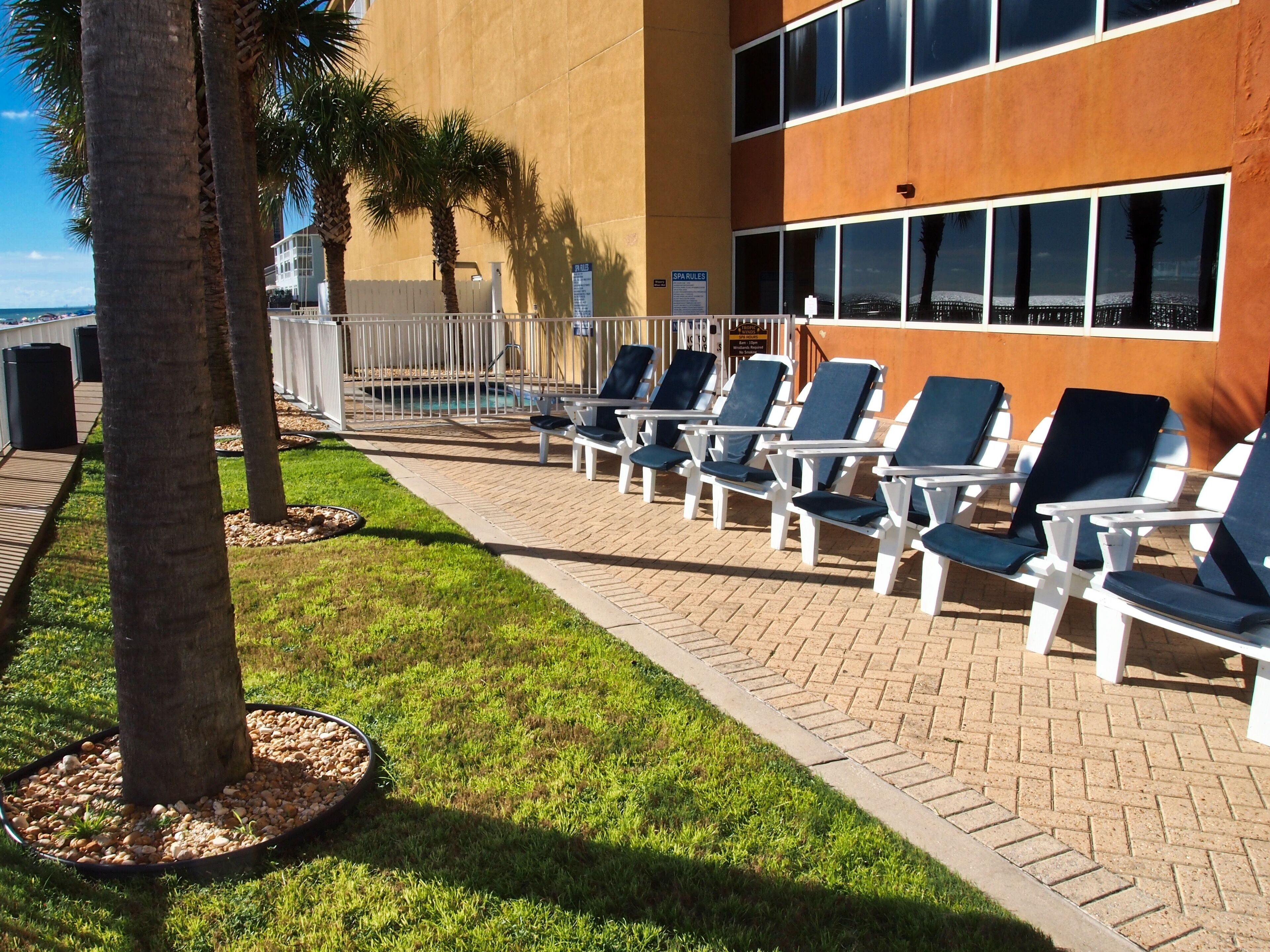 A poolside area with lounge chairs, palm trees, and a building with large windows.