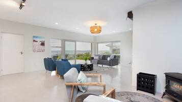 A spacious living room with a fireplace, large windows, and a modern chandelier.