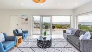A modern living room with two sofas, a coffee table, and a large window with a view of the sea. - Blueview on Silversand (Betty's Bay)