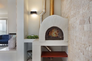 A modern kitchen with a built-in wood-fired oven, a white countertop, and a blue sofa in the adjacent living area.