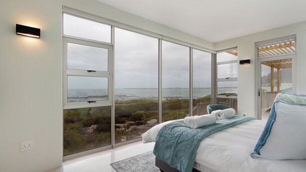 A bedroom with a large sliding glass door leading to a balcony with a view of the sea. - Blueview on Silversand (Betty's Bay)