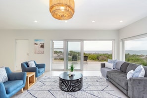 Una sala de estar moderna con dos sofás, una mesita de centro y un ventanal con vistas al mar.