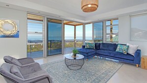 A modern living room with a blue sofa, a grey armchair, and a round coffee table with a plant. - Blueview on Silversand (Betty's Bay)