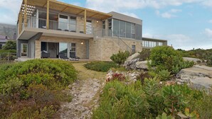 A modern two-story house with a stone facade, large windows, and a wooden balcony. - Blueview on Silversand (Betty's Bay)
