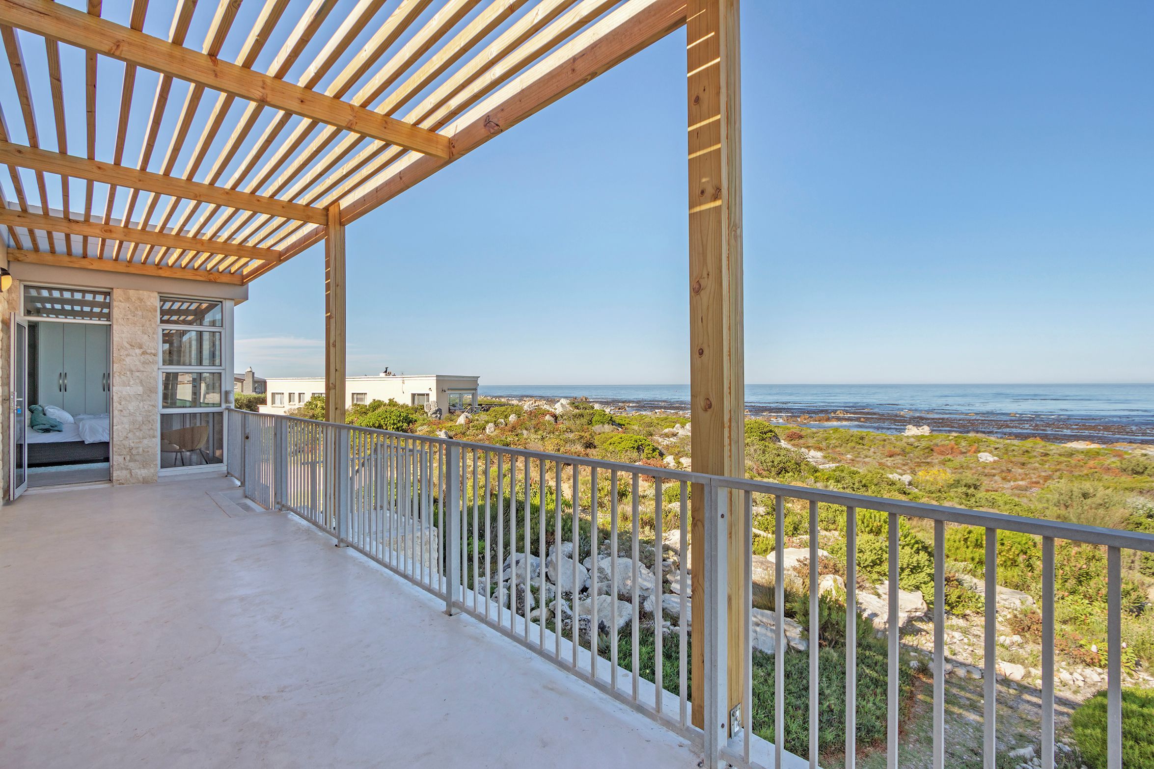 Varanda com vista para o mar, uma estrutura de pérgola e um edifício com porta de vidro.