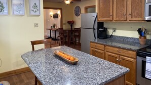 A kitchen with granite countertops, wooden cabinets, a refrigerator, a coffee maker, and a dining area with a table and chairs.