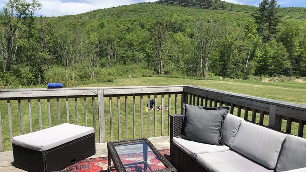 A deck with outdoor furniture, a table, and a view of a forested hillside.