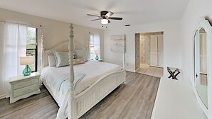 A bedroom with a four-poster bed, a ceiling fan, and a large window with curtains. - Tiki Retreat (North Fort Myers)