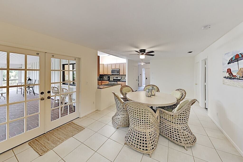 A dining area with wicker chairs and a round table, a ceiling fan, and a view into the kitchen.