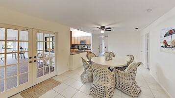 A dining area with wicker chairs and a round table, a ceiling fan, and a view into the kitchen.