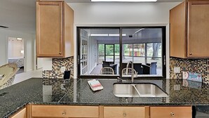 A kitchen with wooden cabinets, a black granite countertop, a sink, and a view of an outdoor patio. - Tiki Retreat (North Fort Myers)