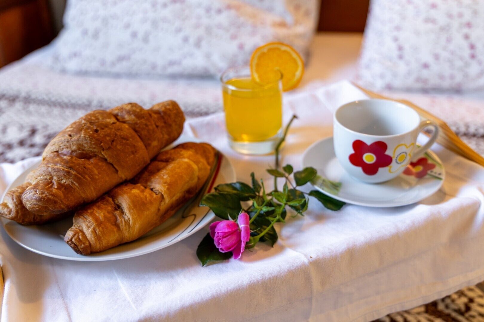 Een ontbijt met croissants, een glas sinaasappelsap en een bloemenbeker op een witte tafelkleed.