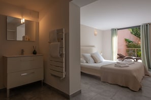 A modern bathroom with a large mirror, a towel rack, and a bedside table. The room has a bed with a beige bedspread and pillows. - Villa T3 du Domaine Zuria (Bonifacio)