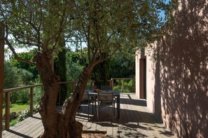 A wooden deck with a table and chairs, surrounded by trees and a building. - Villa T3 du Domaine Zuria (Bonifacio)