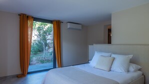 Camera da letto con un grande letto, una porta finestra che si apre su un giardino e un condizionatore d'aria a parete.