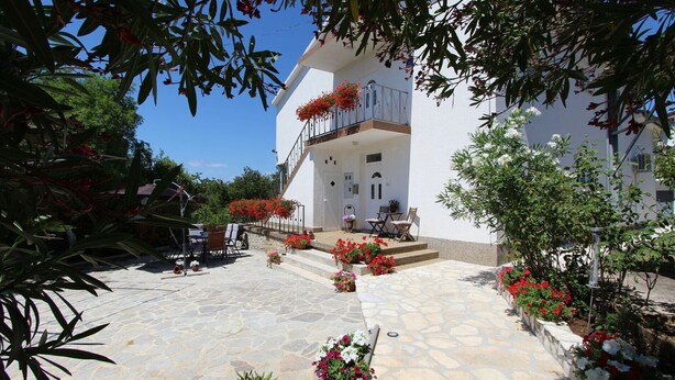 A white building with a stone-paved courtyard, outdoor seating, and potted plants.