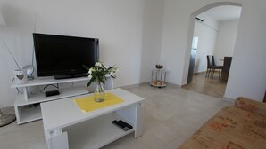 A modern living room with a flat-screen TV, a white coffee table with a vase of flowers, and a sofa.