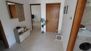 A hallway with a wooden door, a white console table with drawers, a potted plant, and a washing machine.
