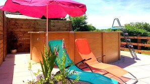 Una terraza de madera con dos sillones y una sombrilla roja, rodeada de vegetación.