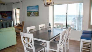 Un comedor con una mesa y sillas, un televisor y vista al océano.