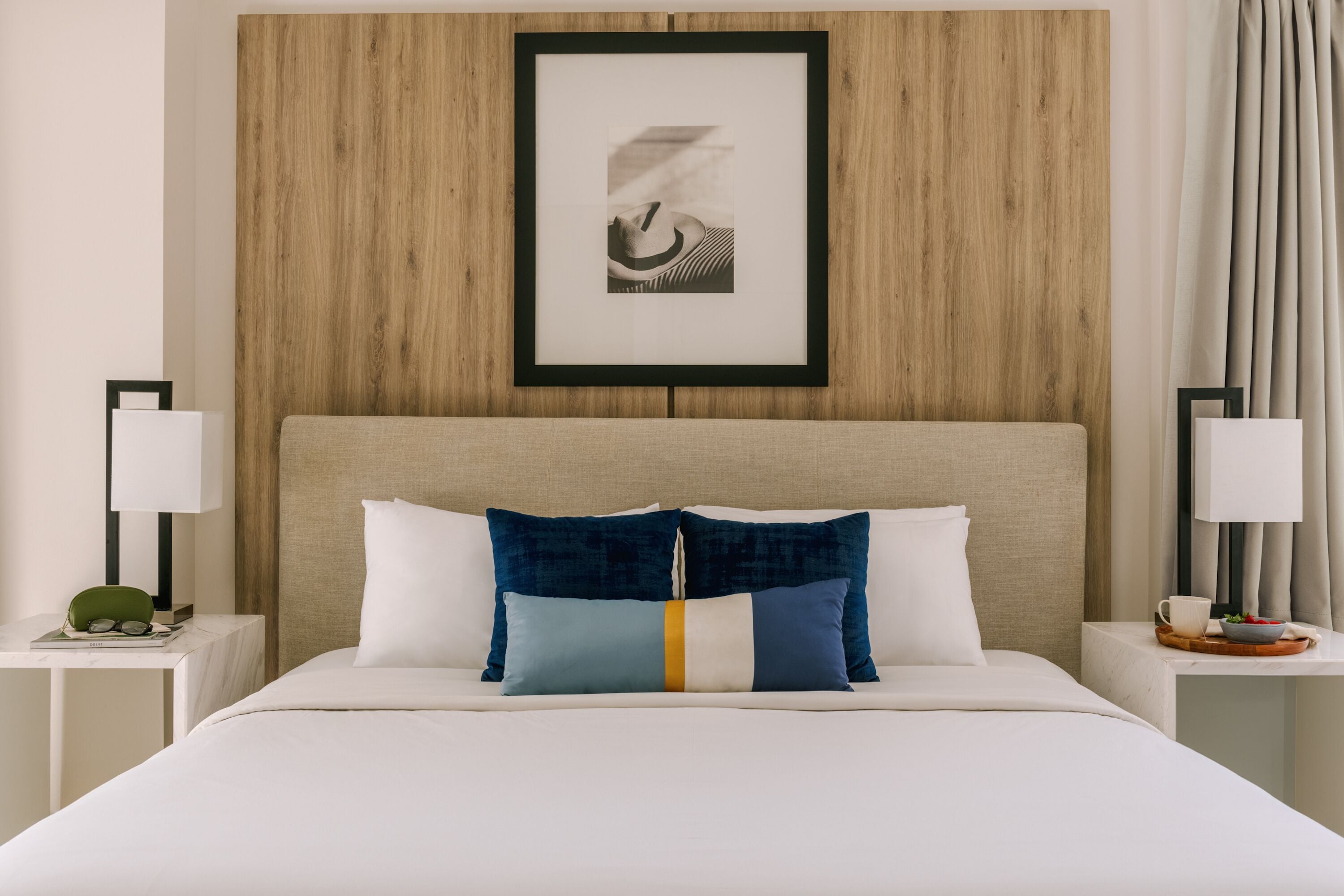 A neatly made bed with white and blue pillows, a wooden headboard, and a framed picture above.