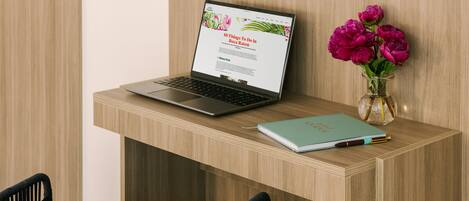 Una laptop sobre un escritorio de madera, junto con un cuaderno y un florero.
