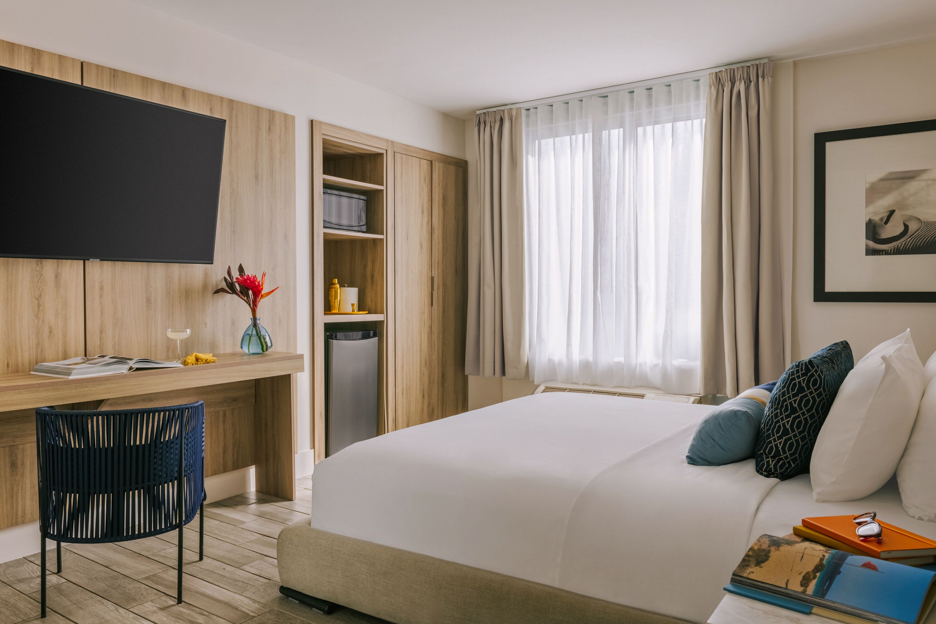 Habitació d'hotel amb llit, escriptori, televisió, minibar i finestra amb cortines.