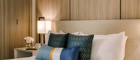 A hotel room with a bed, pillows, a nightstand, a lamp, and a vase with flowers.
