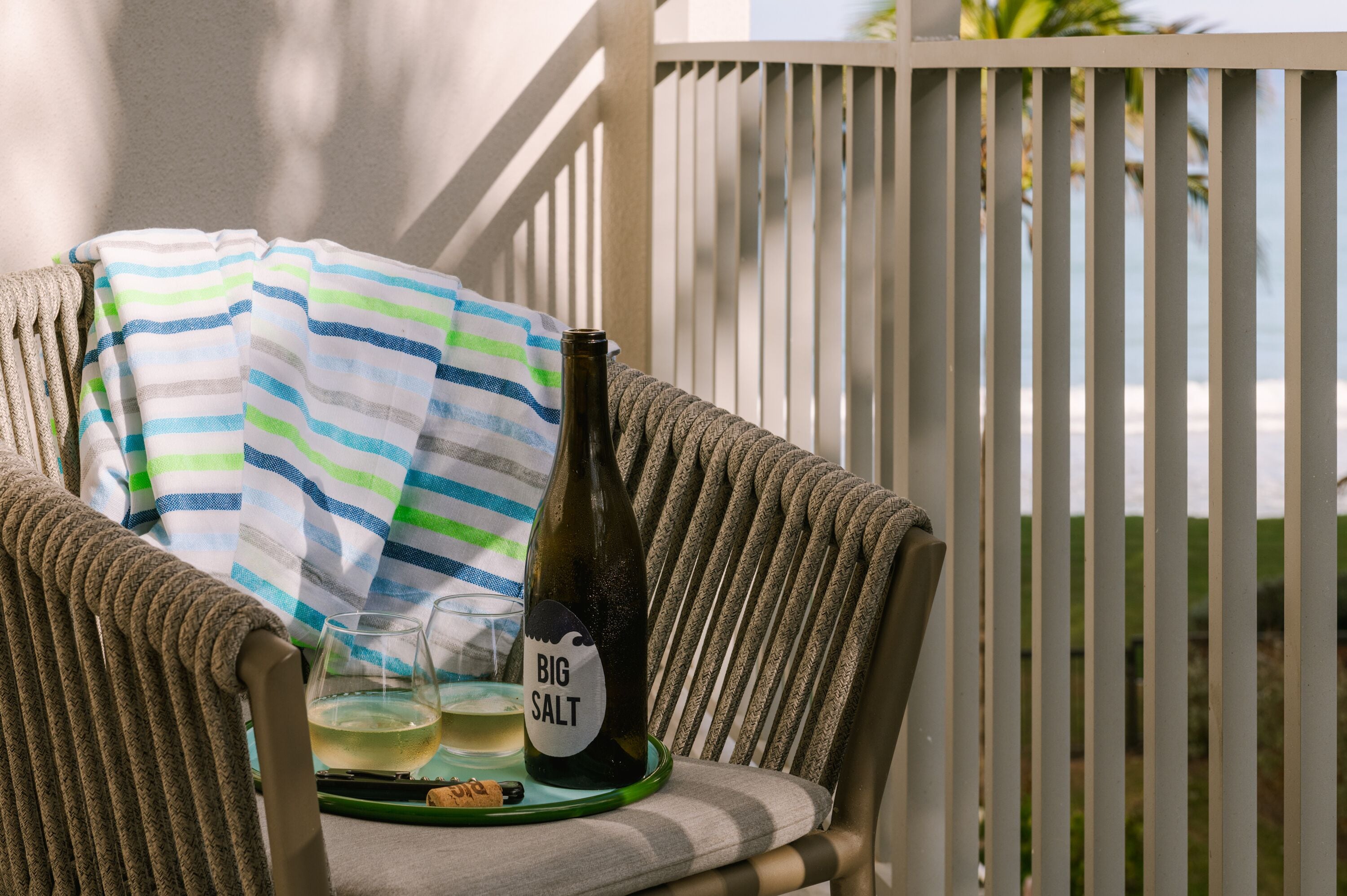 A wicker chair with a striped towel and a bottle of Big Salt wine on a tray.