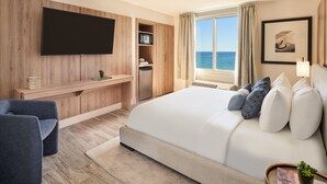 Une chambre d’hôtel moderne dotée d’un grand lit, d’un téléviseur à écran plat fixé au mur, d’une petite kitchenette et offrant une vue sur l’océan.