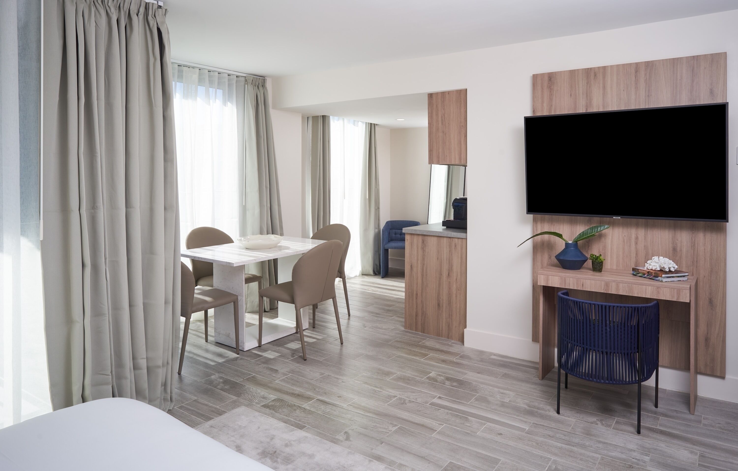 Een moderne hotelkamer met een zithoek, een aan de muur bevestigde televisie en een klein bureau met een plant.