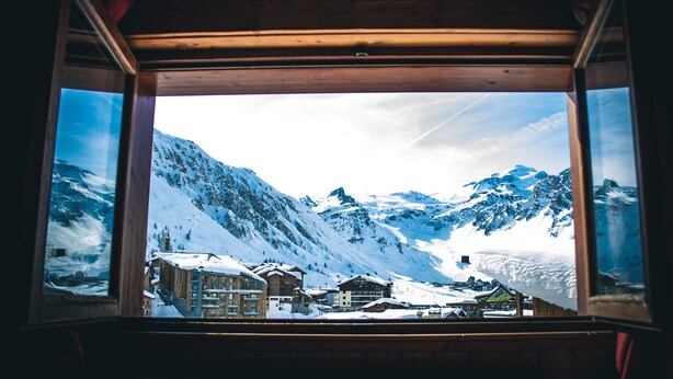 Une vue par la fenêtre sur une station de montagne, avec des bâtiments et des montagnes recouverts de neige.