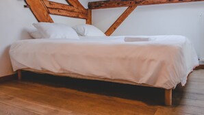 Un lit avec une literie blanche, dans une pièce dotée de poutres en bois et d’un plancher en bois.