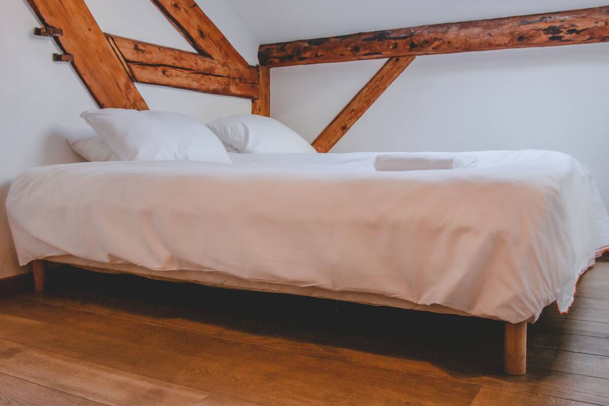 A bed with white bedding in a room with wooden beams and a wooden floor.
