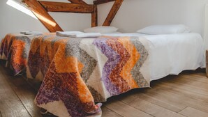 Une chambre confortable située dans les combles, avec des poutres apparentes, un plancher en bois et une couverture colorée sur le lit.