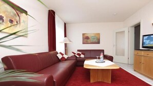 Una sala de estar moderna con un sofá rojo, una mesa de centro de madera y un televisor sobre un mueble.