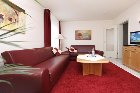 A modern living room with a red sofa, a wooden coffee table, and a television on a stand. - Ferienwohnung Upland 3 (Willingen-Usseln)