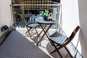 A small outdoor balcony with a round table, two chairs, a potted plant, and a bottle of wine.