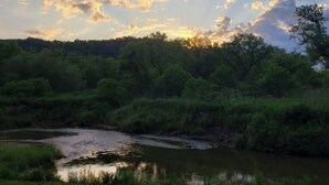 A natural landscape with a river, dense greenery, and a clear sky with sunlight rays. - #6 Blakley Hobbit Campground-Tent spot (Viola)
