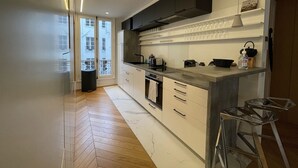 A modern kitchen with white cabinets, a black range hood, and a large window overlooking a cityscape.