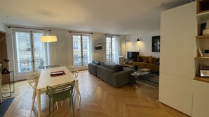 A modern living room with a dining area, a sofa, a TV, and a bookshelf.