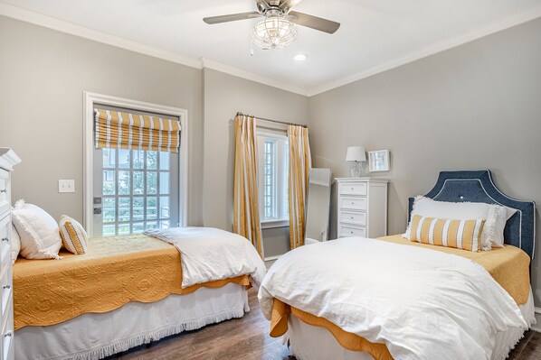 Une chambre avec deux lits, un ventilateur de plafond, une commode et une fenêtre avec des rideaux.