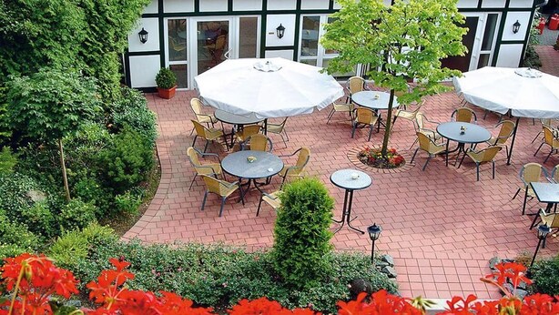 An outdoor patio with round tables and chairs, surrounded by a brick pathway and greenery. - Vacation apartment in Haus Wiesenblume: Apartment 1 (Willingen-Usseln)