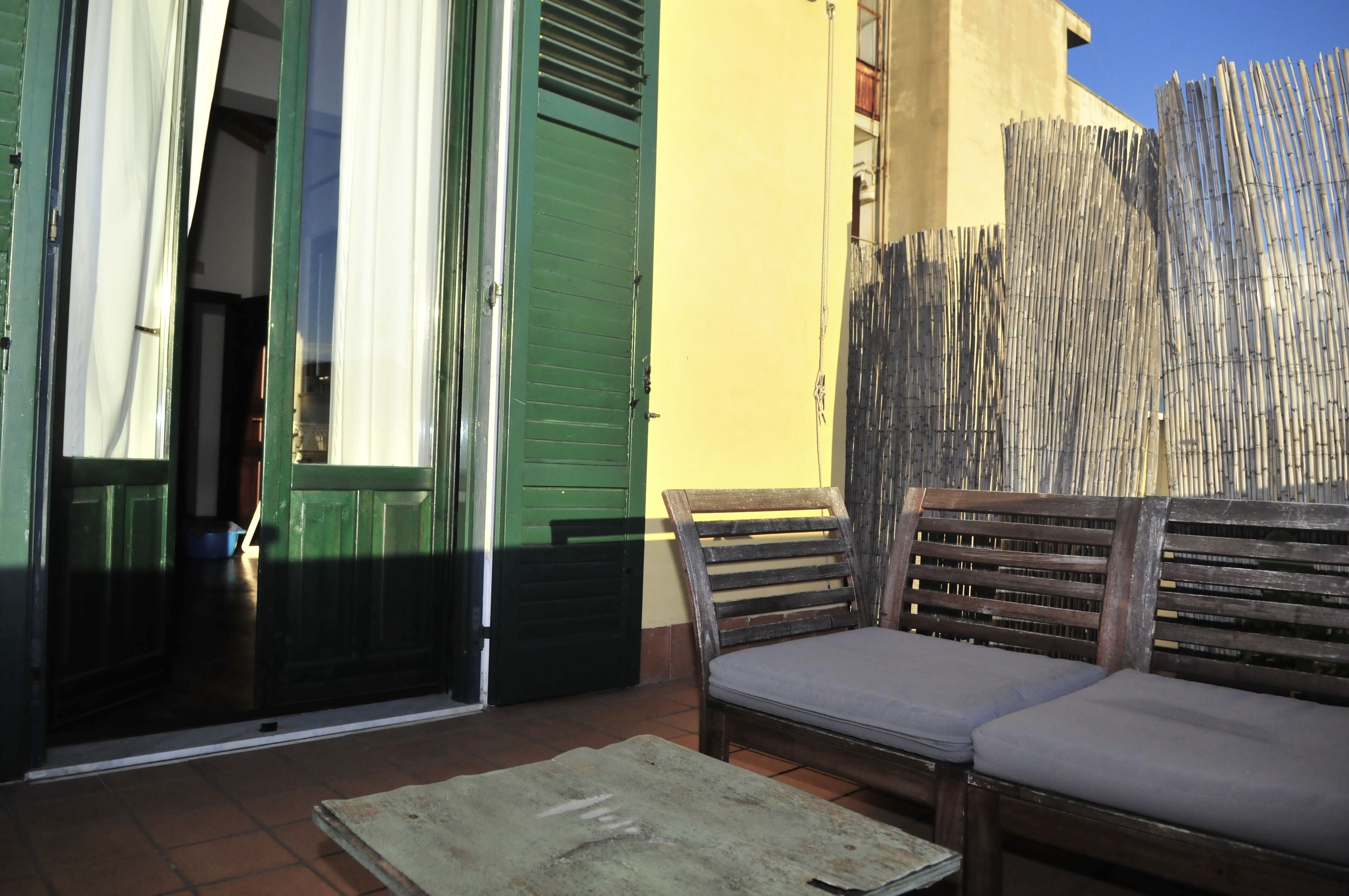 Eine Terrasse mit einer Holzbank und einem Tisch, einer grünen Tür und einem Bambuszaun.