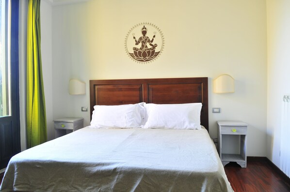 Una cama bien tendida con sábanas blancas, un cabecero de madera y dos mesitas de noche con lámparas.
