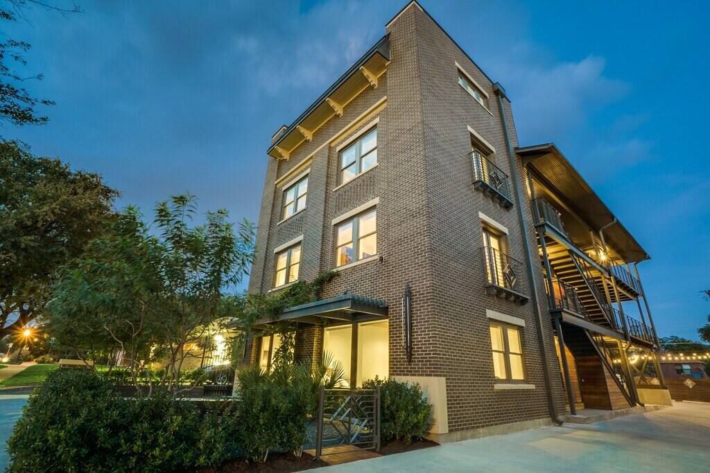 A multi-story building with a brick facade, large windows, and a covered outdoor area with plants.