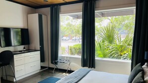 Een hotelkamer met een bed, een bureau met stoel, een televisie en een raam met gordijnen.