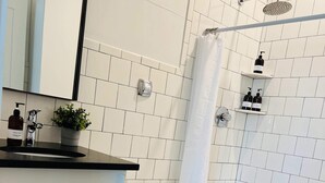 Een moderne badkamer met witte tegels, een douche, toilet, wastafel met spiegel en een kamerplant.